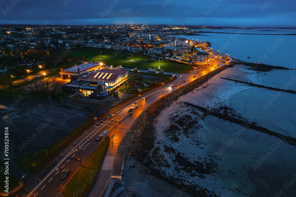 Aerial view on Salthill area of Galway city, Ireland. Night scene with illuminated roads, buildings and city lights and dark sky and ocean. Stunning town view. Warm and cold color toning.