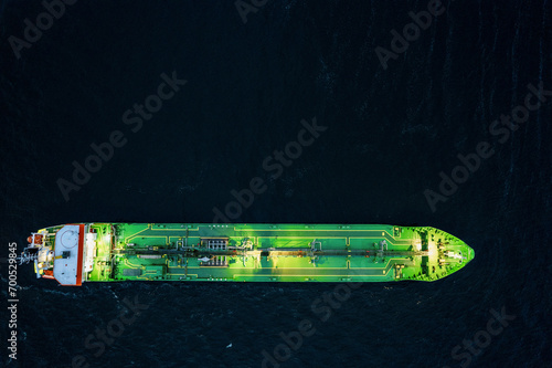 Small illuminated tanker ship with green deck in the dark blue ocean water. Aerial view. Oil and gas transportation and supply. High value goods delivery by water. Logistics and marine trade.