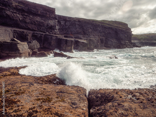 Ocean waves crushing on rough stone coast of rugged Irish coast line with cliffs. Kilkee area, Ireland. Popular travel and tourism area with stunning nature scenery. Dramatic cloudy sky. photo