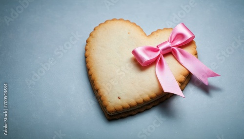  a heart - shaped cookie with a pink bow on a blue background with copy space for the word i love you written in the middle of the cookie and a pink ribbon on the top of the heart.