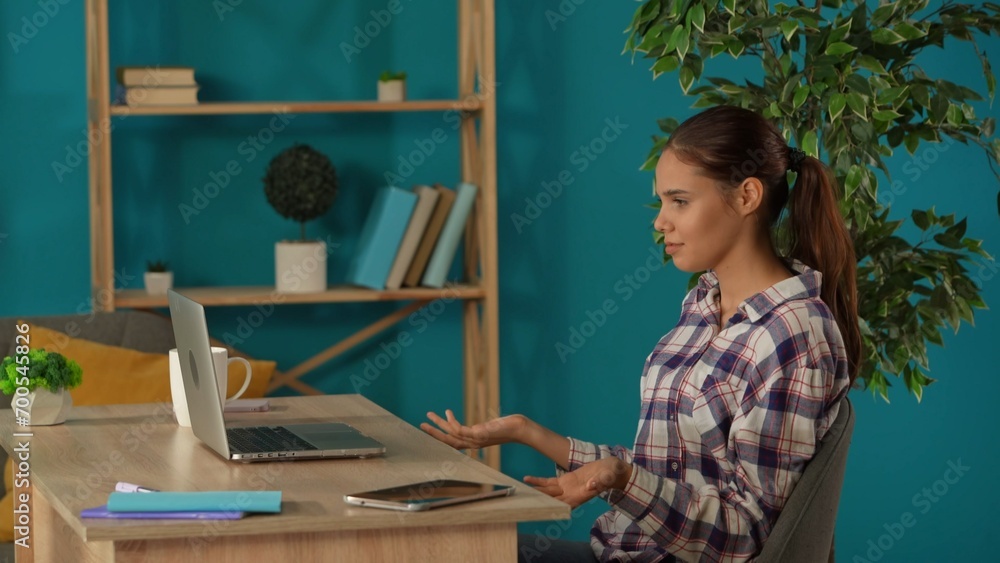 Medium shot capturing a woman having a videocall, talking to somebody on a laptop in her home office. Young female programmer, businesswoman working. Medium shot capturing a woman having a videocall, talking to somebody on a laptop in her home office. Young female programmer, businesswoman working.