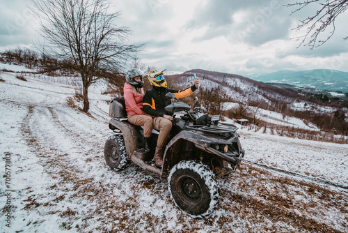  A couple enjoys an adventurous quad ride through the snowy landscape, capturing the thrill of the moment with a selfie on their smartphone amidst the wintry wonderland