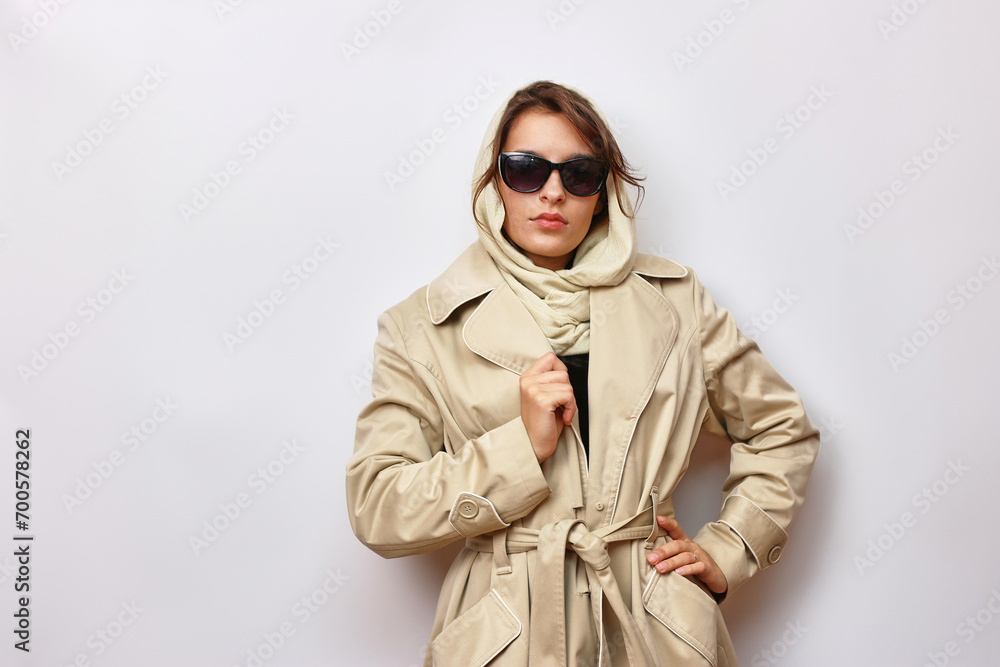 A beautiful girl in sunglasses is dressed in a light autumn raincoat and a scarf.