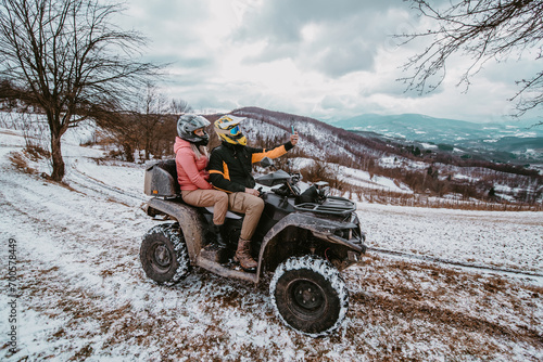  A couple enjoys an adventurous quad ride through the snowy landscape, capturing the thrill of the moment with a selfie on their smartphone amidst the wintry wonderland