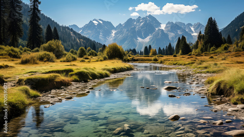A tranquil mountain river flowing through a scenic alpine valley with snow-capped peaks and a clear blue sky in the background.