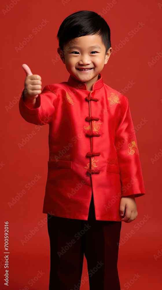 Asian cute boy wearing traditional cheongsam qipao dress with gesture of congratulation isolated on red background. Happy Chinese new year. Asian cute boy wearing traditional cheongsam qipao dress with gesture of congratulation isolated on red background. Happy Chinese new year.