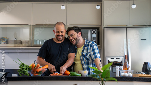 Happy male gay couple standing in kitchen at home preparing together yummy dinner on first dating, male couple chatting enjoy warm conversation and cooking process.
