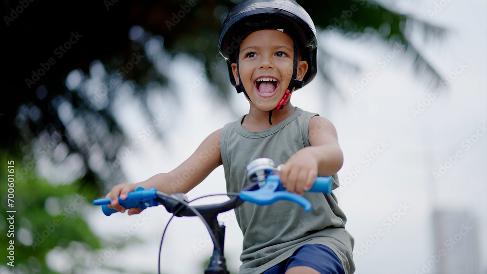 Obraz premium Portrait little cute adorable mixed race toddler boy in safety helmet enjoy having fun riding exercise bike in city park road yard garden forest. Child first bike. Kid outdoors sport summer activities