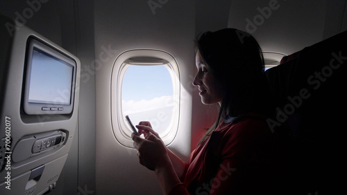 Caucasian female passenger chatting online via cellphone using wifi internet connection on board. Young woman browsing network during flight 