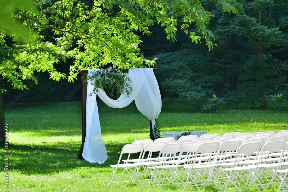 Decorated wedding altar at an outdoor wedding in a garden park with white chairs