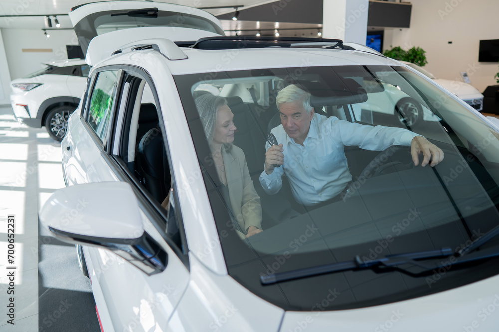 Mature Caucasian couple sitting in a new car and rejoicing at the purchase. View through the windshield. Mature Caucasian couple sitting in a new car and rejoicing at the purchase. View through the windshield.