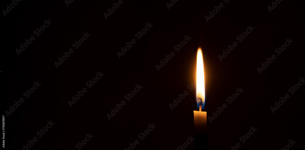 A single burning candle flame or light glowing on a small orange candle on black or dark background on table in church for Christmas, funeral or memorial service with copy space A single burning candle flame or light glowing on a small orange candle on black or dark background on table in church for Christmas, funeral or memorial service with copy space