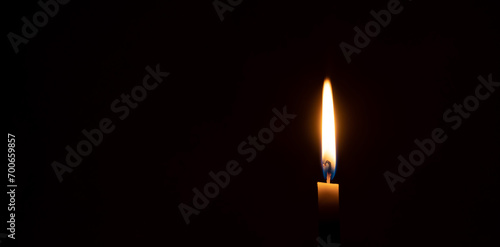 A single burning candle flame or light glowing on a small orange candle on black or dark background on table in church for Christmas, funeral or memorial service with copy space