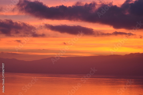 Evening sky over the sea, red discoloured sky after sunset, near Opatija, Croatia. Sunset over the ocean with a silhouette of a headland in the distance and a red orange sky. Sunset backgrounds.