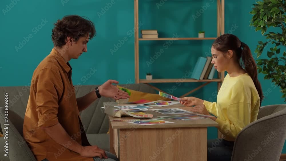 Medium shot capturing a man and a woman working in their home office. Young designers are looking through, comparing the color palettes to apply with their project. Medium shot capturing a man and a woman working in their home office. Young designers are looking through, comparing the color palettes to apply with their project.