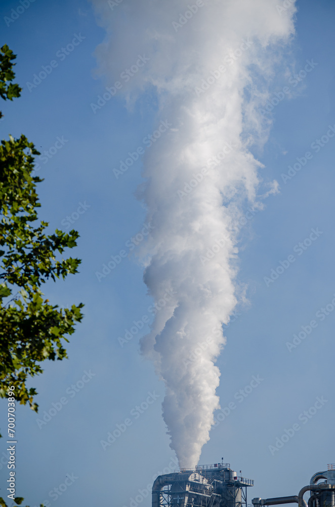 Plume of steam rising from industrial chimney into a blue sky, ecology and climate change concept Plume of steam rising from industrial chimney into a blue sky, ecology and climate change concept
