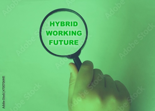 Hand of a child with a magnifier pointing at the sentence “hybrid working future” in a green background .