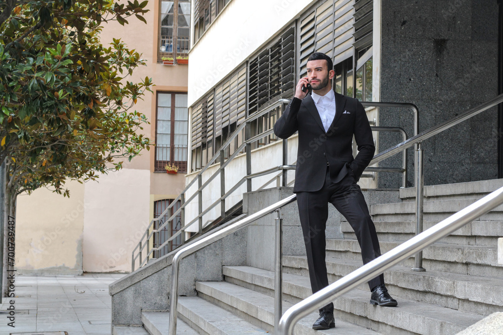Young white man in suit standing on some stairs of an office, talking on the phone, looking away, side view Young white man in suit standing on some stairs of an office, talking on the phone, looking away, side view