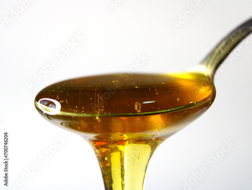 Bee honey dripping from a spoon, isolated on a light background close up.