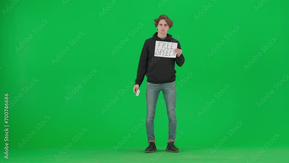 A man with his mouth taped with black tape holds a poster with the inscription Free speech. Protestant man removing tape from his mouth on green screen. Concept of freedom of speech, human rights. A man with his mouth taped with black tape holds a poster with the inscription Free speech. Protestant man removing tape from his mouth on green screen. Concept of freedom of speech, human rights.