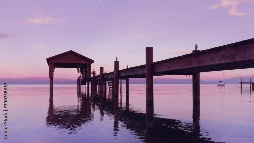 Low angel view of water ripples moving on the lake surface at the dusk. Old pier at the lake shore. Sunset landscape with mountains. Sailboats floating on the background. Calmness concept, 4k footage