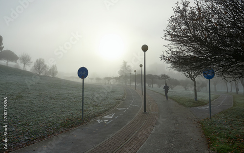 Fototapeta Naklejka Na Ścianę i Meble -  a man practices athletics on a pedestrian track on a cold winter morning with fog and backlight