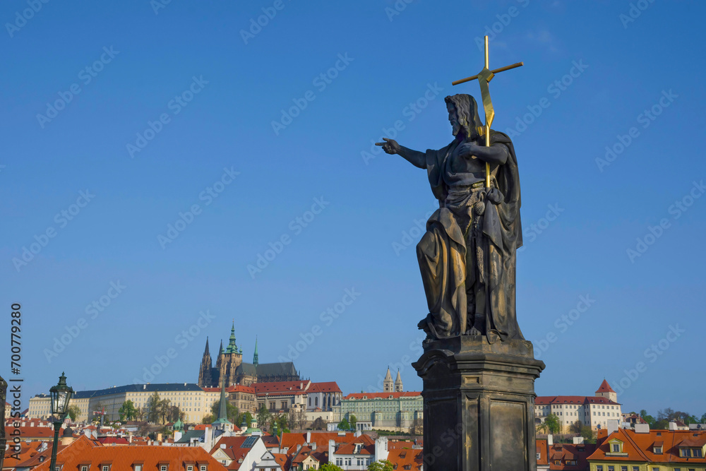 Statue of St. John the Baptist on Charles Bridge, with Hradcany castle and St. Vitus Cathedral in the background, in Prague, Czech Republic, in sunny day