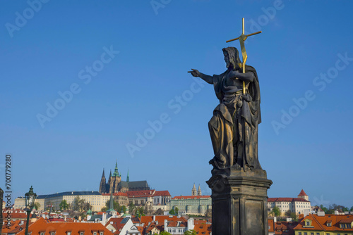 Obraz na płótnie Statue of St. John the Baptist on Charles Bridge, with Hradcany castle and St. Vitus Cathedral in the background, in Prague, Czech Republic, in sunny day w salonie
