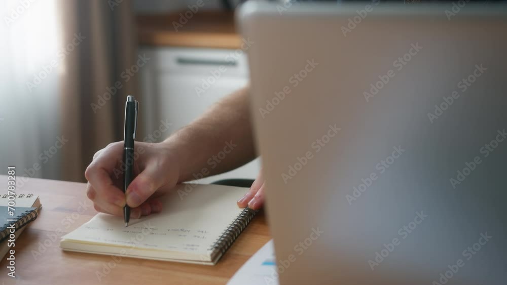 Focused businessman with beanie working at home in the kitchen with his laptop taking notes, doing research. Busy freelancer working on modern tech notebook device Focused businessman with beanie working at home in the kitchen with his laptop taking notes, doing research. Busy freelancer working on modern tech notebook device