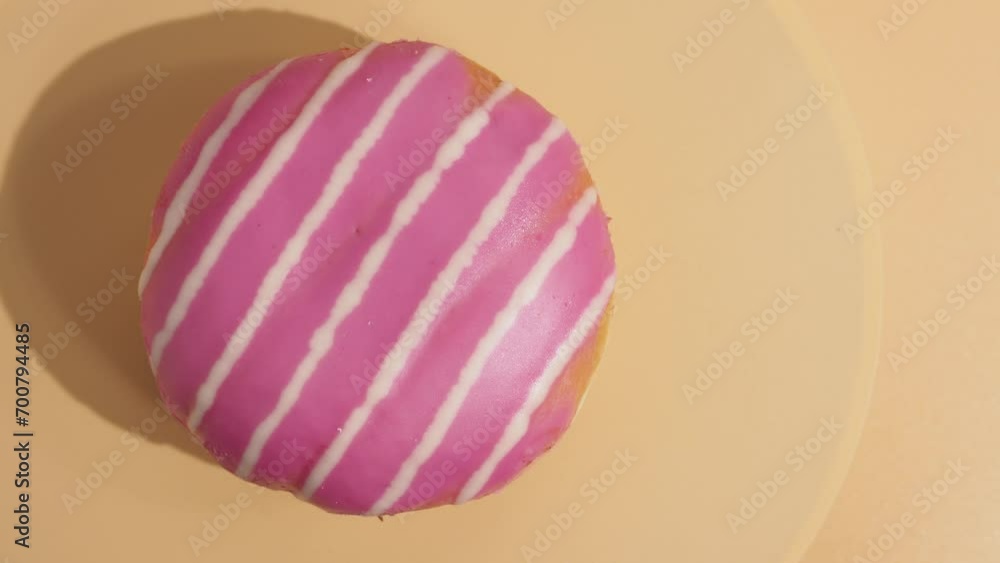 A donut covered with red sugar icing rotates on an orange background. Sweet bun close-up. A donut covered with red sugar icing rotates on an orange background. Sweet bun close-up.