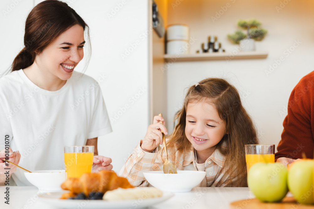 Beautiful young mother and her little daughter having breakfast together sitting at table in kitchen Beautiful young mother and her little daughter having breakfast together sitting at table in kitchen