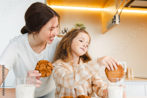 Beautiful woman, mother and her little mother holding oatmeal cookies, dipping in milk in kitchen