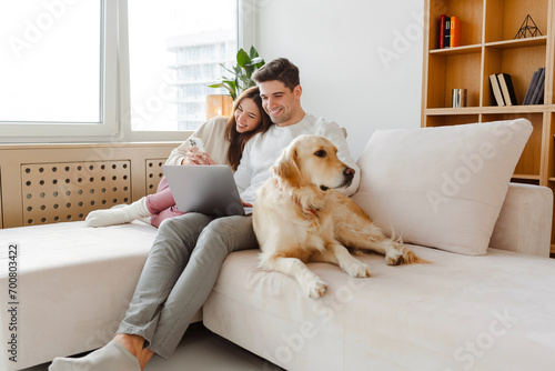 Happy young couple using laptop, man holding mobile phone, hugging dog. Online shopping concept photo
