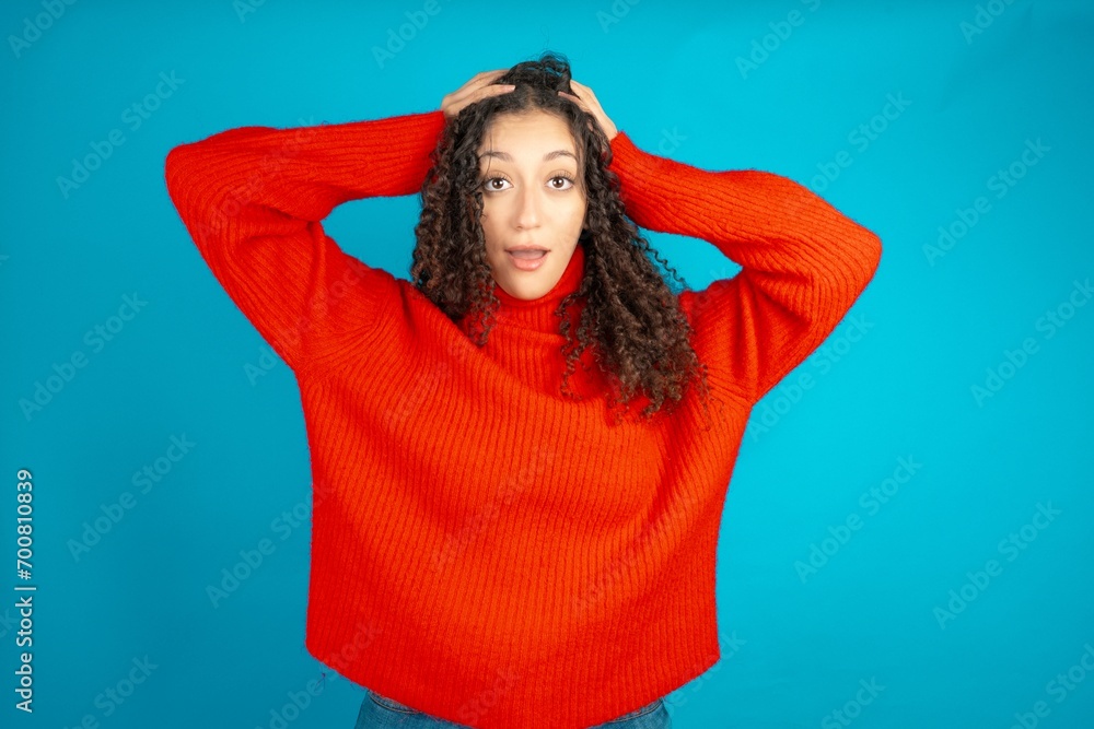 Cheerful overjoyed beautiful teen girl wearing red knitted sweater reacts rising hands over head after receiving great news. Cheerful overjoyed beautiful teen girl wearing red knitted sweater reacts rising hands over head after receiving great news.