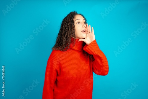 beautiful teen girl wearing red knitted sweater look empty space holding hand face and screaming or calling someone.