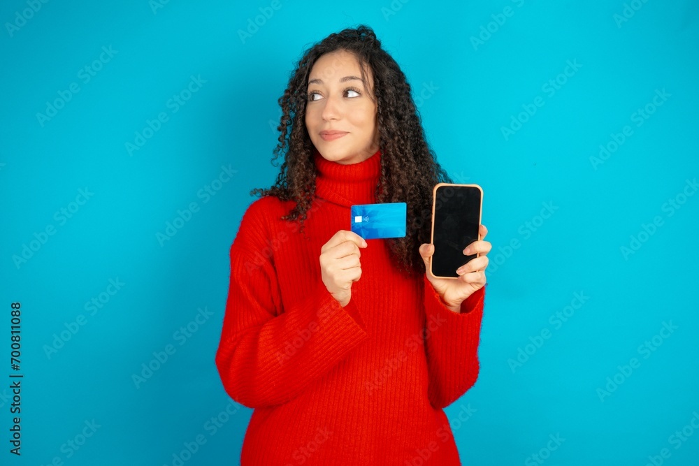 beautiful teen woman wearing red knitted jacket holding bank card modern device looking empty space beautiful teen woman wearing red knitted jacket holding bank card modern device looking empty space