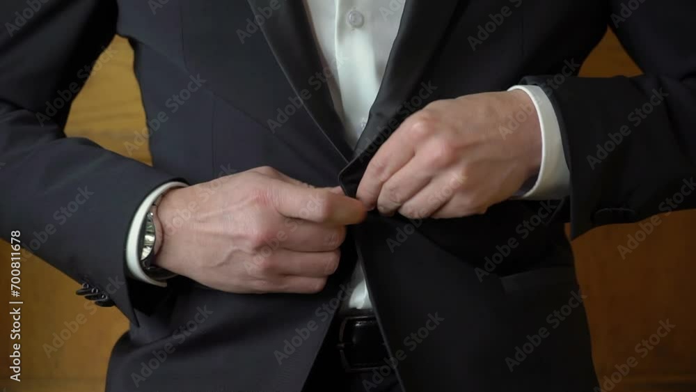 A close up of hands buttoning a suit. Man put on black jacket. Groom in wedding day or businessman. Male in white shirt indoors. A close up of hands buttoning a suit. Man put on black jacket. Groom in wedding day or businessman. Male in white shirt indoors.