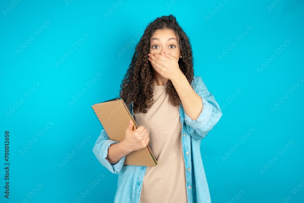 Vivacious beautiful arab student carries notebooks , giggles joyfully, covers mouth, has natural laughter, hears positive story or funny anecdote Vivacious beautiful arab student carries notebooks , giggles joyfully, covers mouth, has natural laughter, hears positive story or funny anecdote