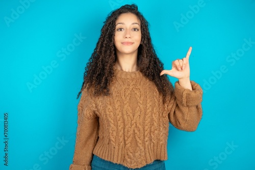 Beautiful teen girl wearing knitted sweater over blue background showing up number six Liu with fingers gesture in sign Chinese language photo