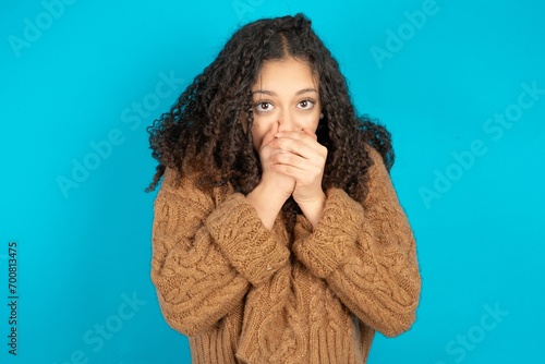 Beautiful teen girl wearing knitted sweater over blue background holding oneself, feels very cold outside, hopes that will not get cold