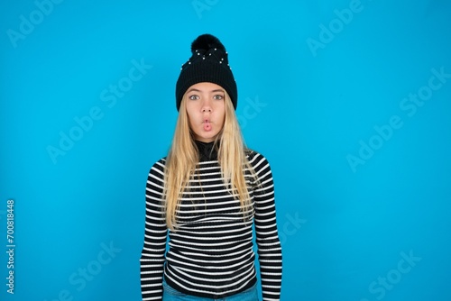 Teen caucasian girl wearing striped sweater and woolly hat making fish face with lips, crazy and comical gesture. Funny expression. photo
