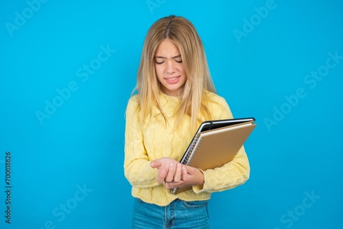 Beautiful kid girl wearing yellow sweater holding notebook Suffering pain on hands and fingers, arthritis inflammation
