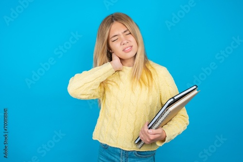 Beautiful kid girl wearing yellow sweater holding notebook Suffering of neck ache injury, touching neck with hand, muscular pain