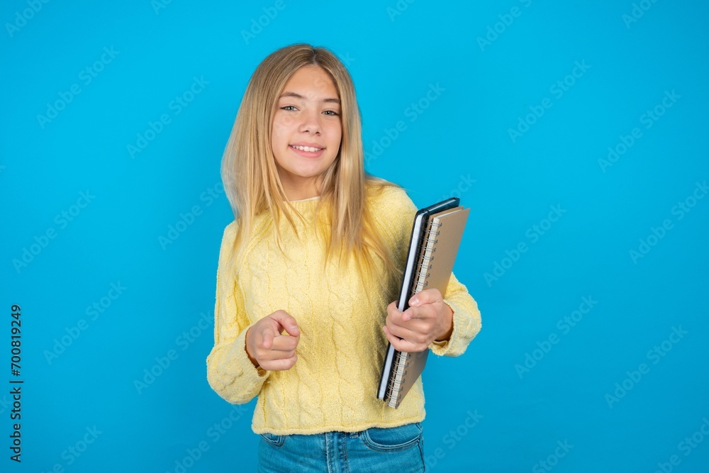 Beautiful kid girl wearing yellow sweater holding notebook pointing fingers to camera with happy and funny face. Good energy and vibes. Beautiful kid girl wearing yellow sweater holding notebook pointing fingers to camera with happy and funny face. Good energy and vibes.