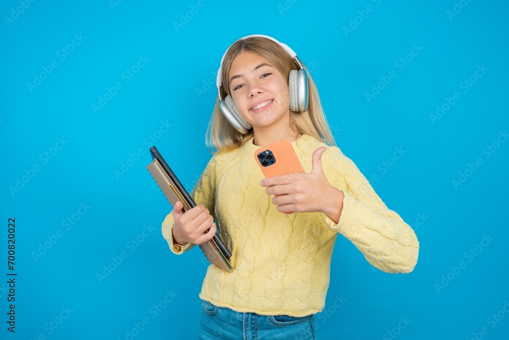 Portrait of Beautiful kid girl wearing yellow sweater holding notebook using and texting with smartphone happy with big smile doing ok sign, thumb up with fingers, excellent sign Portrait of Beautiful kid girl wearing yellow sweater holding notebook using and texting with smartphone happy with big smile doing ok sign, thumb up with fingers, excellent sign