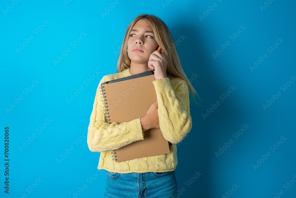 Sad Beautiful kid girl wearing yellow sweater holding notebook talking on smartphone. Communication concept. Sad Beautiful kid girl wearing yellow sweater holding notebook talking on smartphone. Communication concept.
