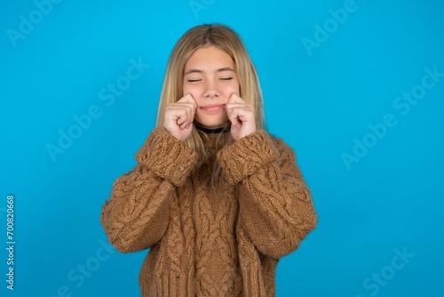 Pleased beautiful caucasian teen girl wearing yellow sweater with closed eyes keeps hands near cheeks and smiles tenderly imagines something very pleasant photo