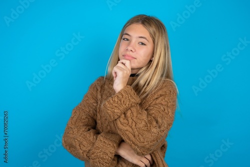 beautiful caucasian teen girl wearing yellow sweater looking confident at the camera smiling with crossed arms and hand raised on chin. Thinking positive.