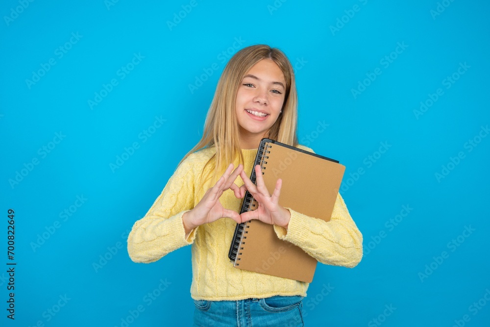 Fototapeta premium Serious beautiful caucasian teen girl wearing yellow sweater keeps hands crossed stands in thoughtful pose concentrated somewhere