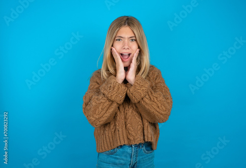 Upset beautiful caucasian teen girl wearing brown sweater touching face with two hands